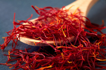 Saffron spice threads (strands) in wooden spoon on black background