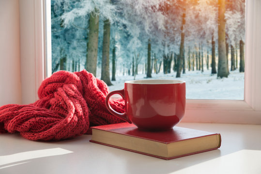 Cup of hot coffee and cozy knitted scarf on wooden table in front of glitter background with snowflakes overlay