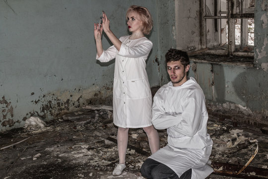 Asylum nurse or doctor with a syringe in hand is preparing to give an injection to an insane psycho patient in a straitjacket, inside of abandoned ruined hospital. Some horror movie scene