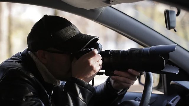 Private detective man sitting inside car and photographing with dslr camera