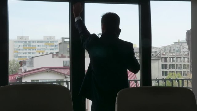Silhouette of businessman talking on the phone and looking outside his office window. Zoom out dolly slider 4K footage