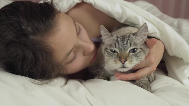 Happy teen girl kisses and talks with Thai cat in bed stock footage video