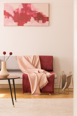 Abstract painting on the empty white wall of elegant living room with grey couch with pastel pink and burgundy blankets