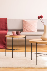 Coffee tables with coffee cups and vase with flowers in bright living room interior with grey sofa,...