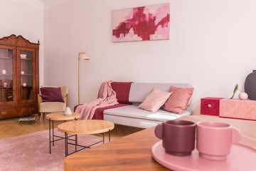 Closeup of two coffee cups on the table in elegant living room with grey couch with pastel pink pillows, stylish armchair and vintage cabinet