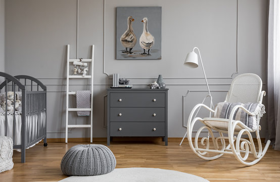 Grey pouf on white carpet inelegant baby bedroom interior with white and grey furniture, real photo