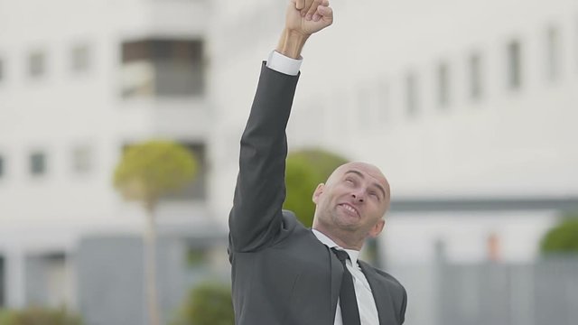 Happy businessman showing yes gesture on street. Front view of successful manager  triumphing near office building. Success concept