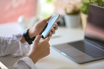 Close-up female hand holding and using mobile phone in a her office.