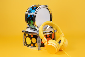 Yellow headphones and mini drum kit on the yellow background. Toy drums.