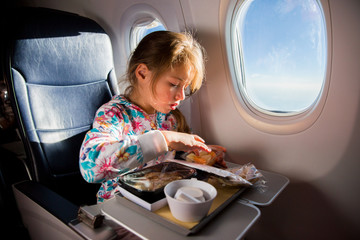 Child eating pancakes in airplane. Little girl having breakfast while flying in aircraft. Blue sky and sun outside the window