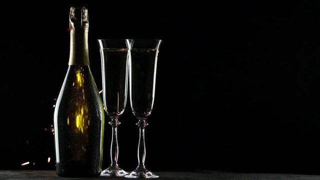 Still-life with a bottle of champagne and glasses. Sparklers on a black background. Slow motion video.