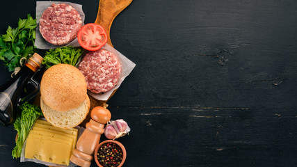Preparation of burger. Meat, fresh vegetables, tomatoes, onions. On a black wooden background. Top view. Free copy space.