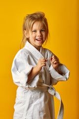 Little serious girl wearing white fighter kimono and standing in pose on yellow background © pavlovski