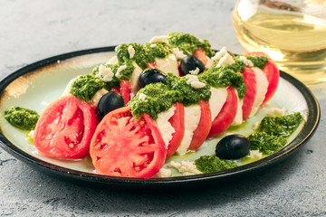 Tomato and mozzarella caprese salad and pesto sauce with olives on gray table