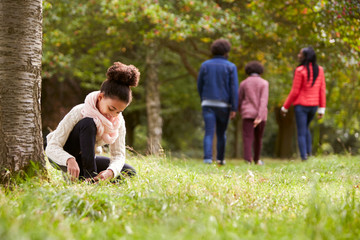 Mixed race girl kneeling in the park to tie her shoe, her family walking in the background, low...