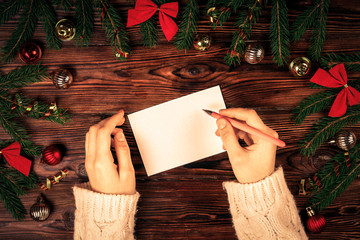 Female hands writing letter to Santa Claus on wooden background with christmas gifts and decoration...