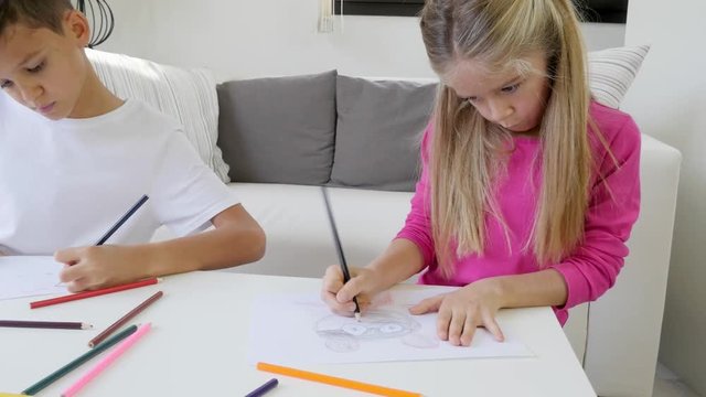 two beautiful young kids boy and girl drawing on a white paper with color pencil