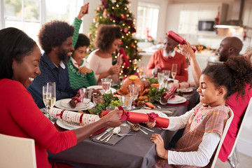 Mixed race, multi generation family having fun pulling crackers at the Christmas dinner table