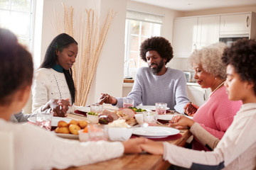 Multi generation mixed race family holding hands and saying grace before eating their Sunday dinner