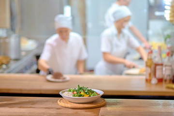 Fresh healthy salad on wooden table. View from above with copy space. cooks in the kitchen as a blurred background behind.