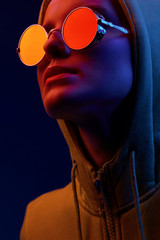 Neon close up portrait of young woman in round sunglasses and hoodie. Studio shot - 233554967