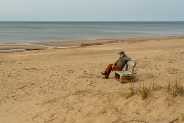 Fototapeta na wymiar man sitting on a bench on the beach, cloudy, autumn