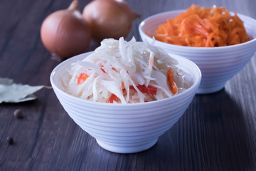 Marinated cabbage and carrots in white bowls on a brown wooden table. The concept of pickled and fermented vegetables.