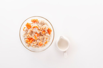 Oatmeal with pumpkin and nuts in a glass plate and a jug with milk on a white background. Copy space. Top view
