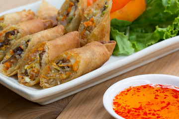 Deep fried spring rolls, Por Pieer Tod or Fried spring rolls (Thai Spring Roll) on white dish on wooden table,Thai and Chinese people.