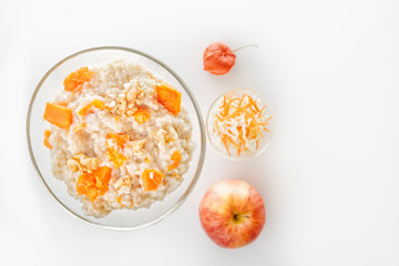 Oatmeal with pumpkin and nuts in a glass plate and fresh apple on a white background. Copy space. Top view
