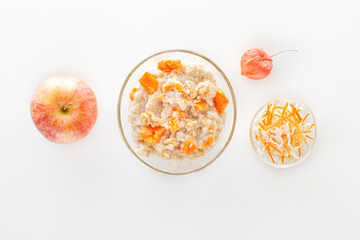 Oatmeal with pumpkin and nuts in a glass plate and fresh apple on a white background. Copy space. Top view