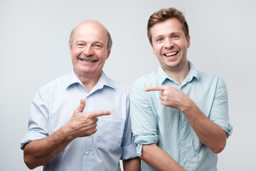 Two men hugging, pointing finger each other and looking at camera with shocked face.