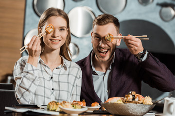 Lovely couple having fun while eating sushi rolls in restaurant