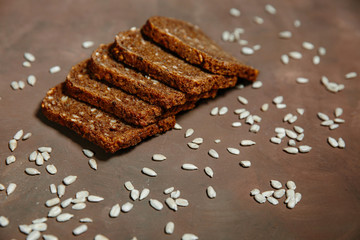 Composition of dark bread Slices with cereals and sunflower seeds on brown background