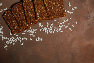 Composition of dark bread Slices with cereals and sunflower seeds on brown background