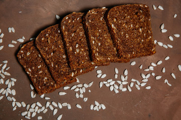 Composition of dark bread Slices with cereals and sunflower seeds on brown background