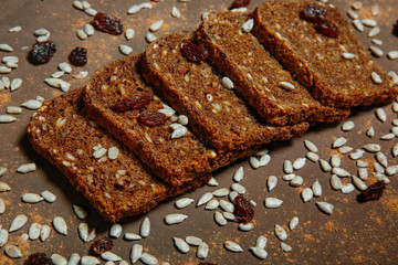 Top view of bread with different seeds (pumpkin, poppy, flax, sunflower, sesame, millet, raisins) on a brown background.
