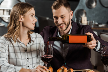 Attractive smiling couple having dinner and man pouring wine in glass in restaurant
