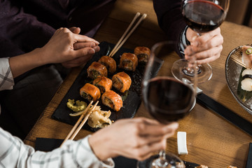 Partial view of couple holding hands while drinking wine and eating sushi in restaurant - Powered by Adobe