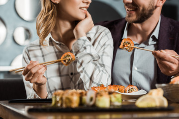 Cropped view of smiling happy couple eating sushi in restaurant