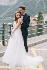 Fototapeta premium A beautiful wedding couple walks on the lake and mountains background in a fairy Austrian town, Hallstatt.