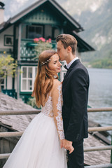 A beautiful wedding couple walks on the lake and mountains background in a fairy Austrian town, Hallstatt.