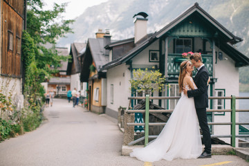 A beautiful wedding couple walks on the lake and mountains background in a fairy Austrian town,...
