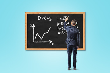 Businessman writing formula on chalkboard or blackboard on blue background