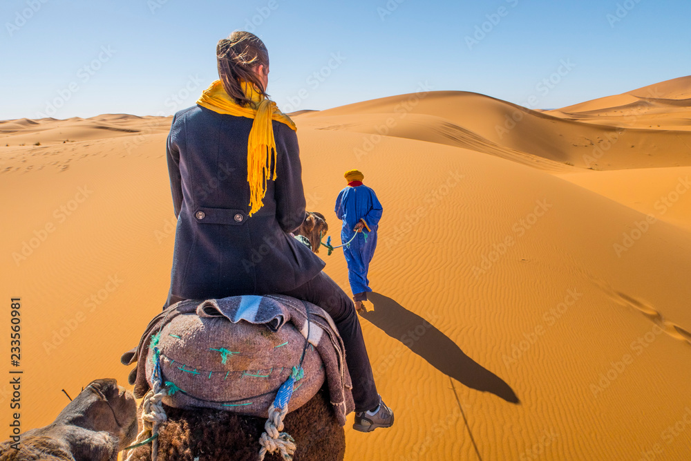 Wall mural berber nomad and a young girl riding camel in sahara desert, morocco