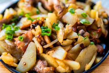 Roasted potato in frying pan with meat and green leek