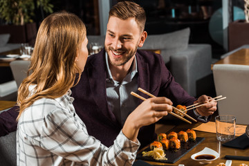 Beautiful happy couple eating sushi rolls in restaurant