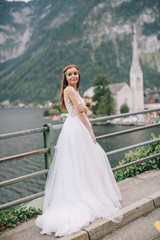 Fototapeta na wymiar A beautiful bride walks near a lake on a mountains background in a fairy Austrian town, Hallstatt.