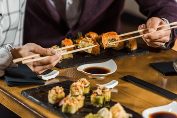 Cropped view of people eating sushi with chopsticks in restaurant