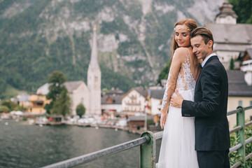 A beautiful wedding couple walks on a background old cathedral, lake and mountains in a fairy Austrian town, Hallstatt.